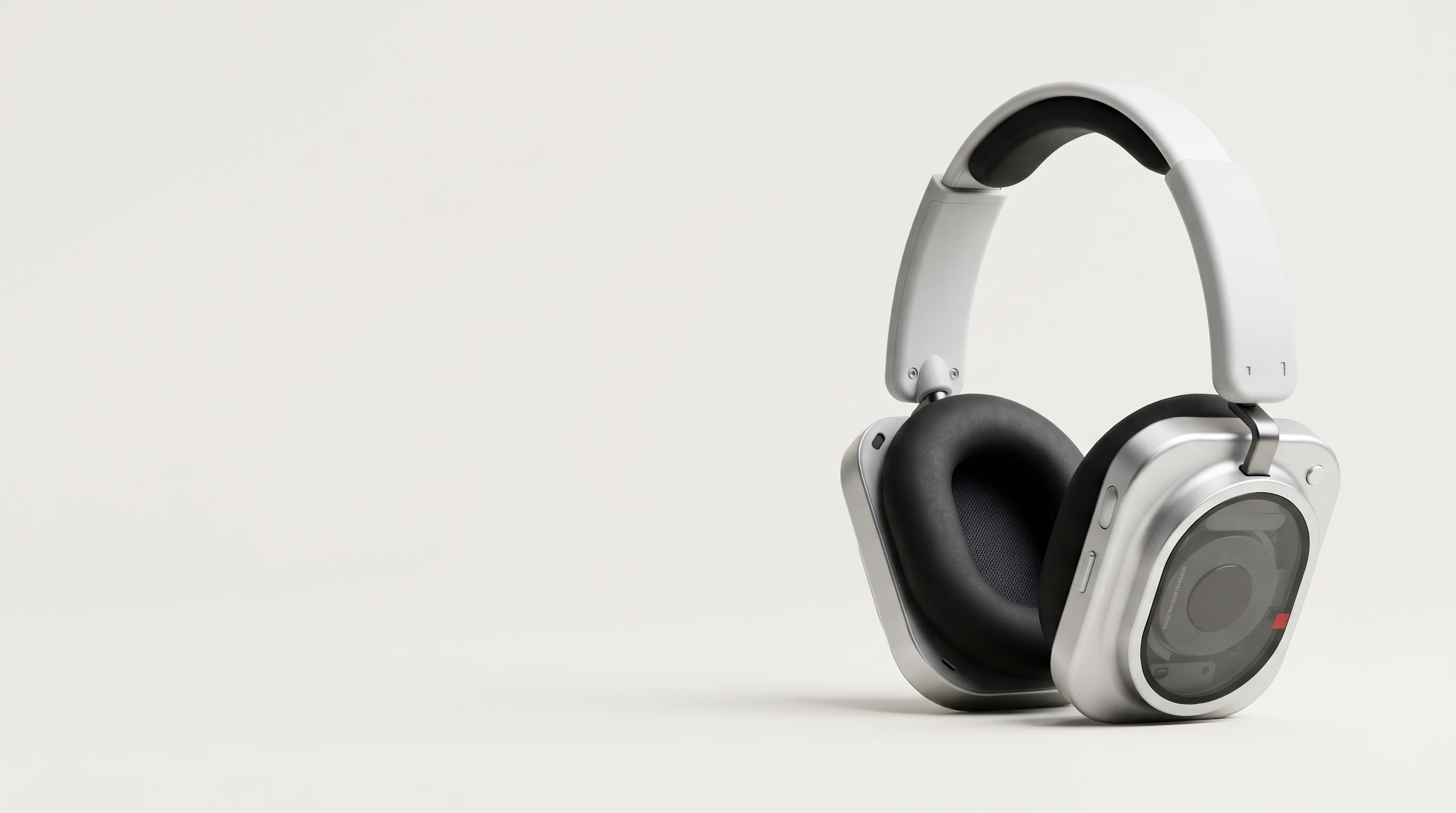White Headphone (1) Pro with aluminium ear cups and a transparent window over the driver, on a light grey ground, with empty space on the left